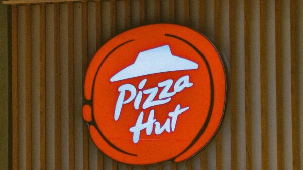 Illuminated Pizza Hut sign on a wooden storefront captured in daylight.