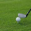 Golf club poised to hit a golf ball on a tee, set against a lush green grass background.