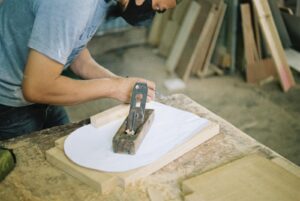 Carpenter woodworking with a hand plane on a wooden surface indoors.
