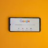 Smartphone displaying Google search page on a vibrant yellow background.
