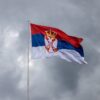 Serbian flag on pole against overcast sky, symbolizing national pride.