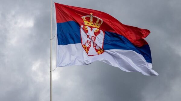Serbian flag on pole against overcast sky, symbolizing national pride.