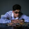 Portrait of a man in sunglasses leaning over a table covered with various currencies.