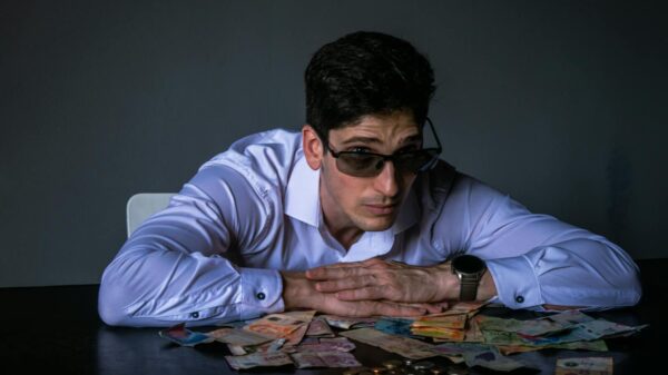 Portrait of a man in sunglasses leaning over a table covered with various currencies.
