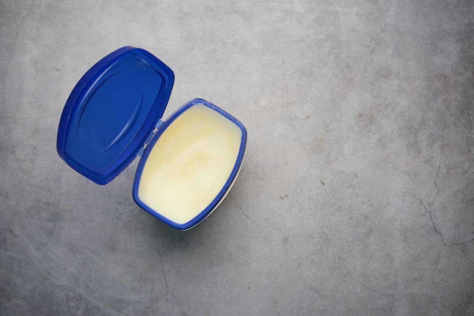 Open blue plastic container with creamy substance on a solid gray background.