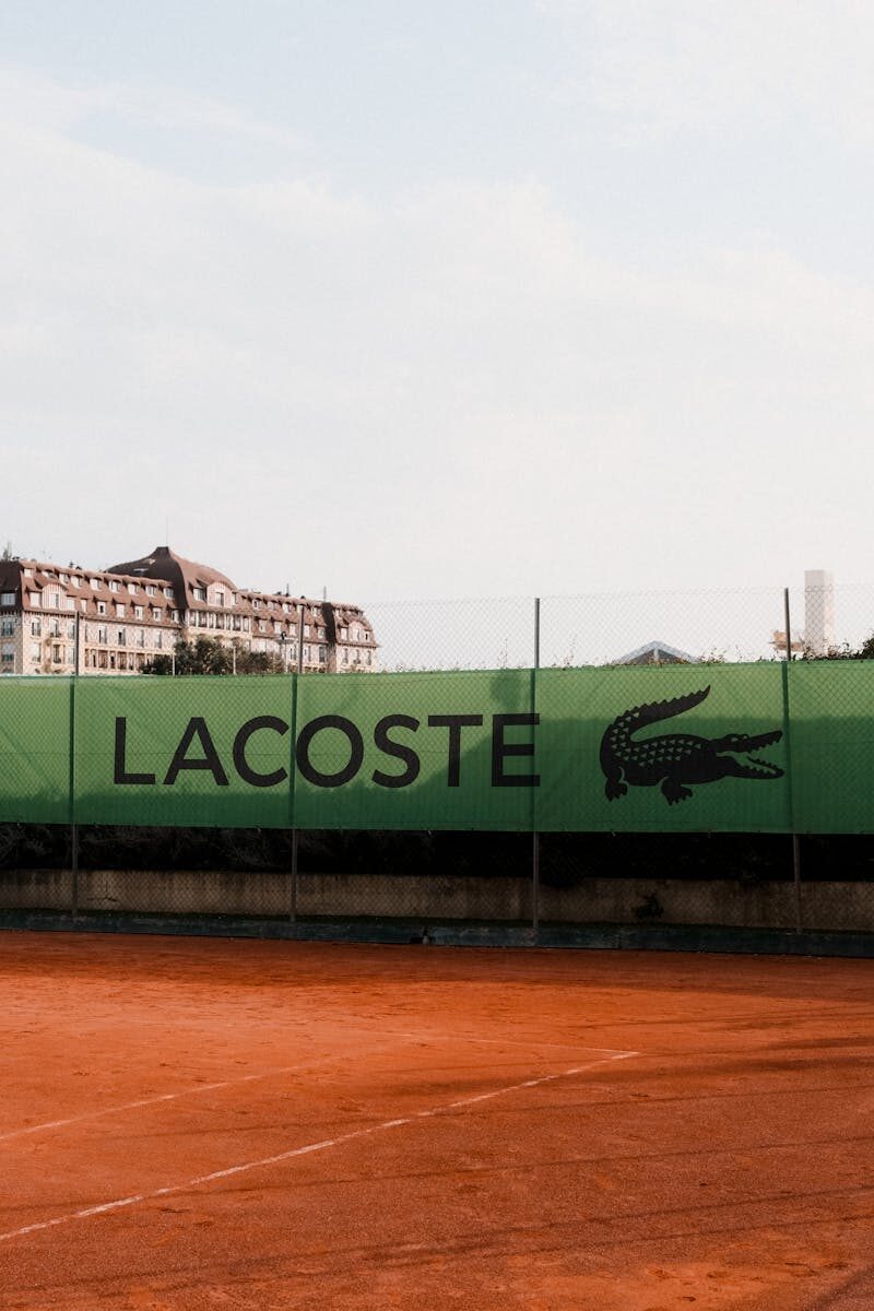 Lacoste branded banner on an outdoor tennis court under a clear sky, showcasing sports advertising.