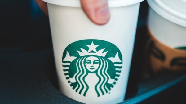 Close-up image of a hand holding a Starbucks coffee cup in a car's cup holder.