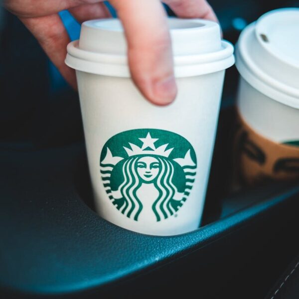 Close-up image of a hand holding a Starbucks coffee cup in a car's cup holder.