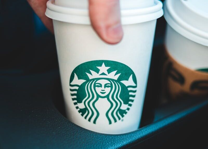 Close-up image of a hand holding a Starbucks coffee cup in a car's cup holder.