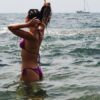 A woman in a bikini enjoying a sunny summer day in the ocean, with a distant sailboat.