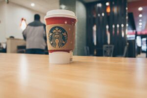 Close-up of a Starbucks coffee cup on a wooden table in a cozy café setting.