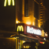 A McDonald's restaurant with glowing neon signage at night, bustling with activity.