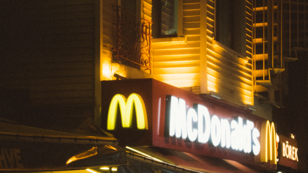 A McDonald's restaurant with glowing neon signage at night, bustling with activity.