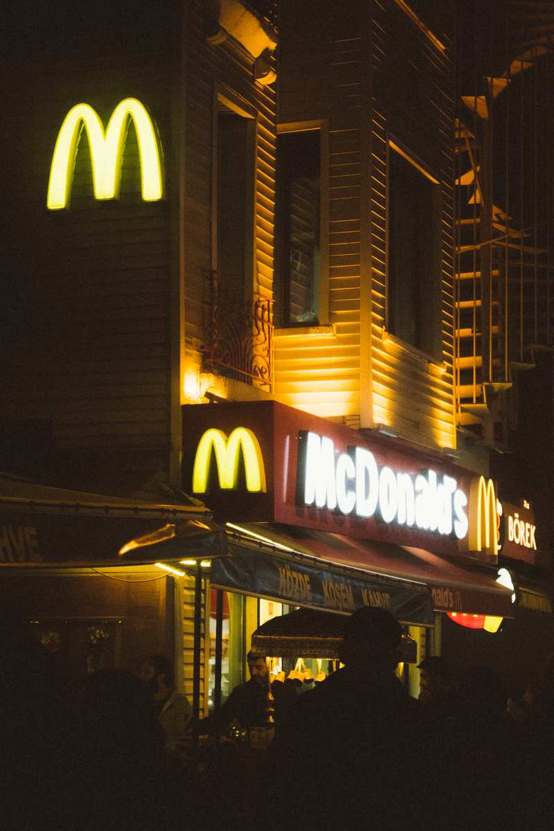 A McDonald's restaurant with glowing neon signage at night, bustling with activity.
