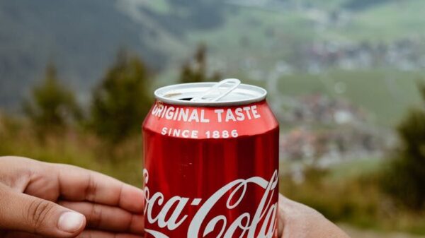 Hands sharing a Coca-Cola can with a scenic mountain backdrop.