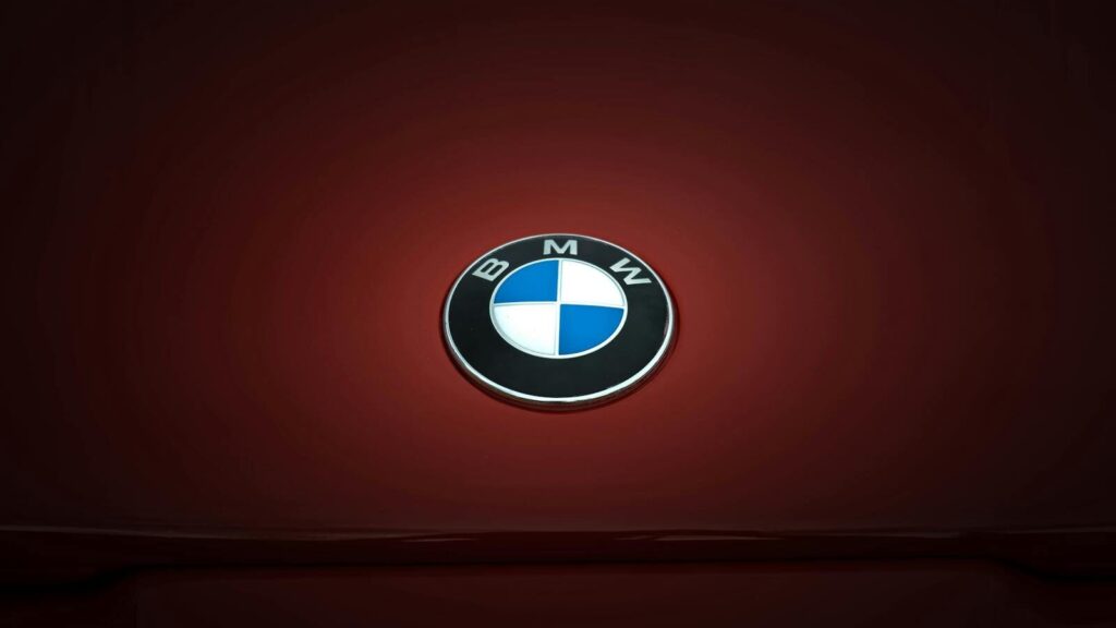 Close-up of BMW emblem on a glossy red vehicle surface, emphasizing modern design.