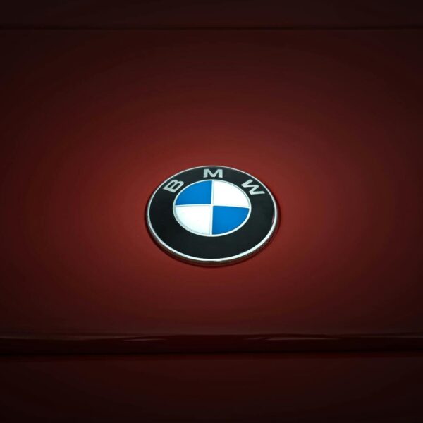 Close-up of BMW emblem on a glossy red vehicle surface, emphasizing modern design.