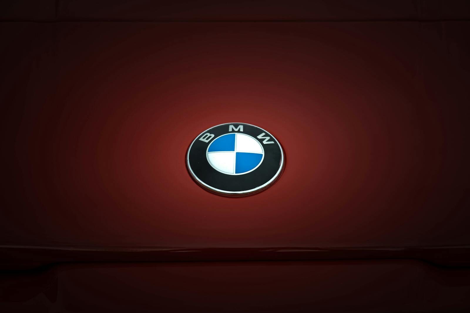 Close-up of BMW emblem on a glossy red vehicle surface, emphasizing modern design.