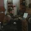 A man focused on using a laptop in a workshop environment, surrounded by tools.