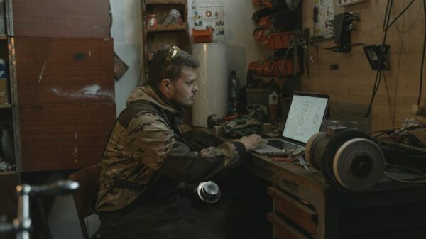 A man focused on using a laptop in a workshop environment, surrounded by tools.