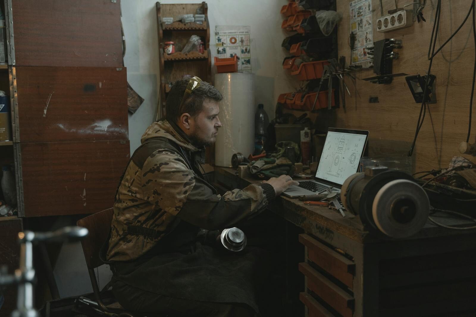 A man focused on using a laptop in a workshop environment, surrounded by tools.