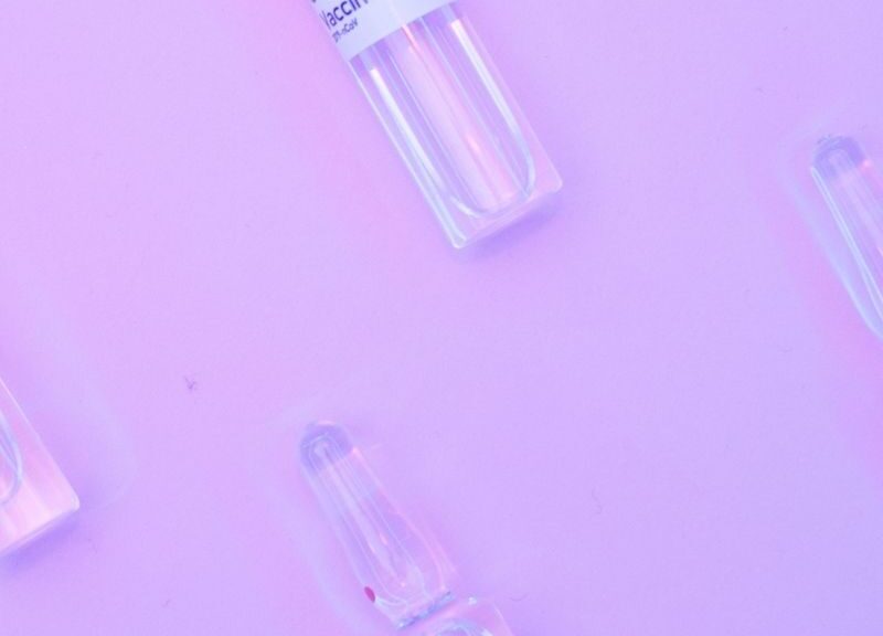 From above small glass vials with vaccine against COVID 19 arranged on purple background