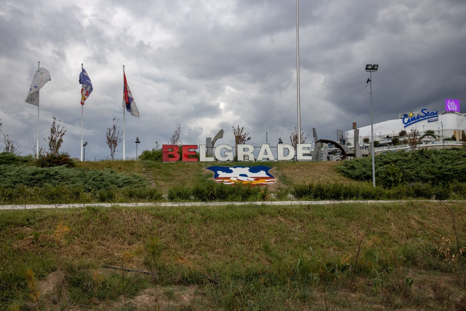 Large Belgrade sign in a park setting with flags on a cloudy day, Serbia