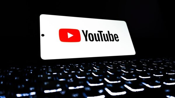 YouTube app icon displayed on a smartphone over an illuminated keyboard, representing digital media and online streaming.