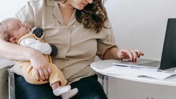 Concentrated mom sitting on chair with cute baby and browsing laptop while working remotely on maternity leave