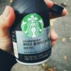 Person holding a bottle of Starbucks Pike Place Roast black coffee outdoors in autumn.