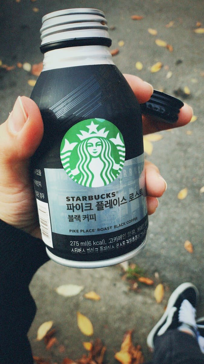 Person holding a bottle of Starbucks Pike Place Roast black coffee outdoors in autumn.