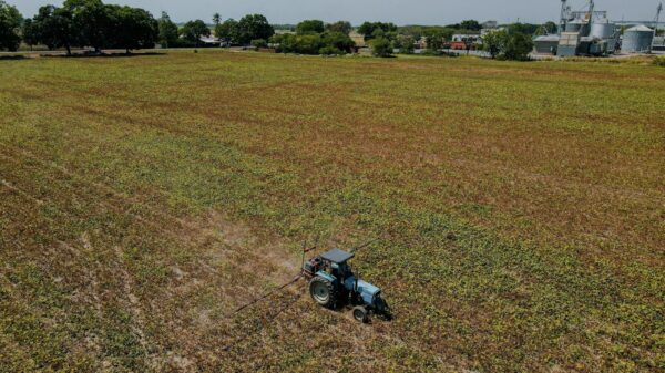 Aerial view of a tractor operating in a large farmland under a clear sky, highlighting agricultural activity.