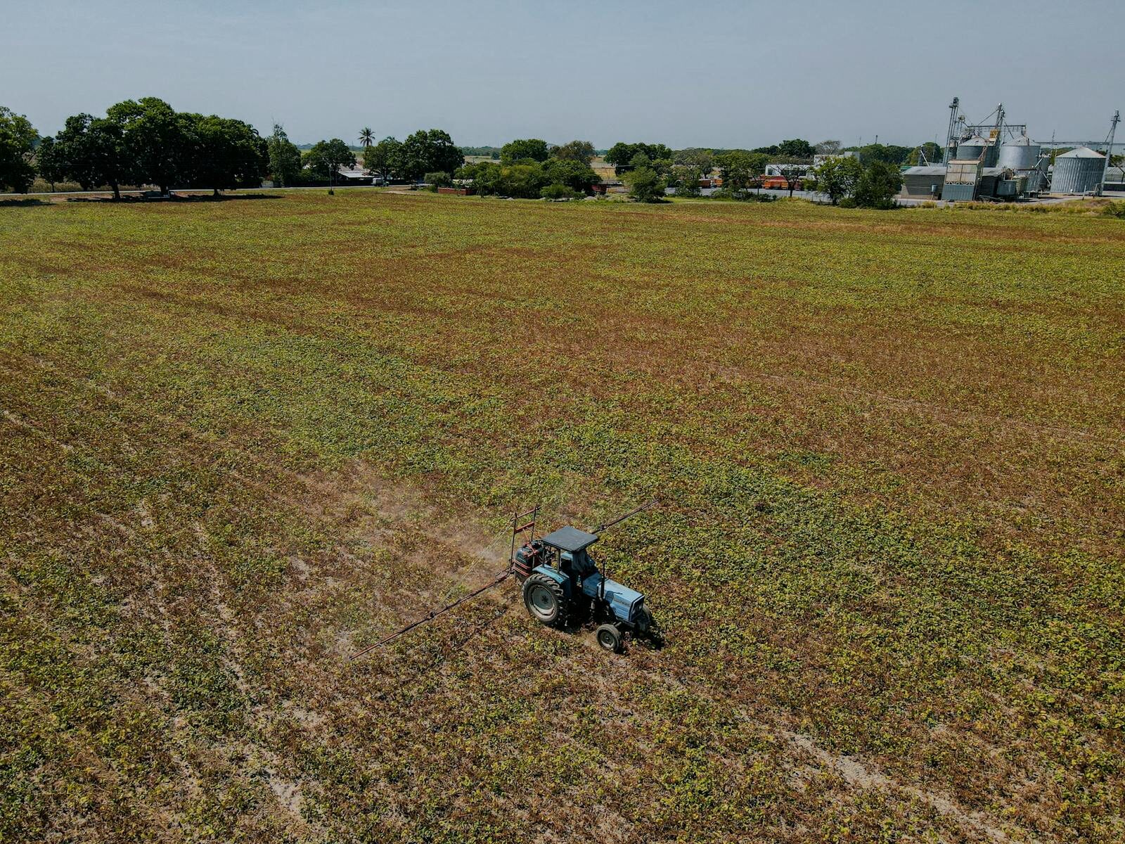 Aerial view of a tractor operating in a large farmland under a clear sky, highlighting agricultural activity.