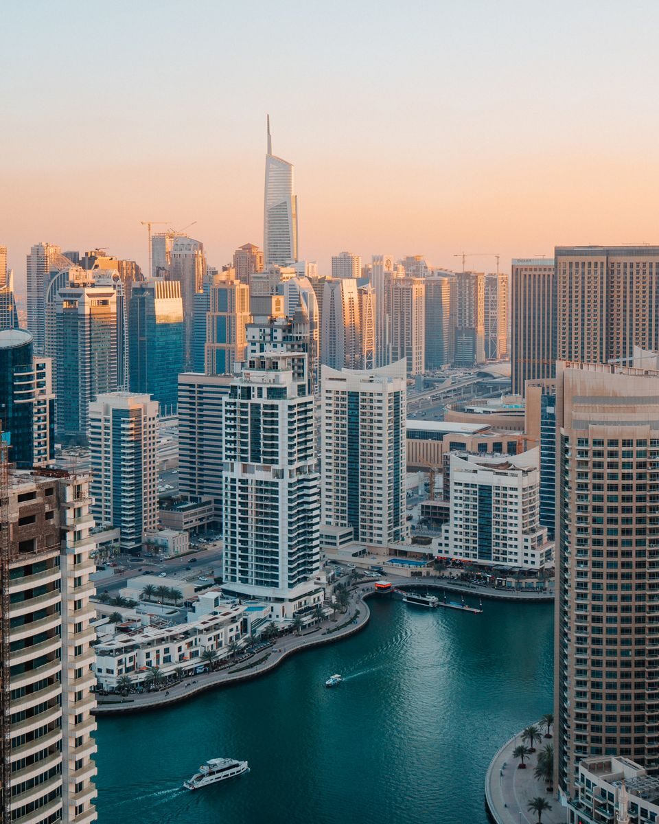 Aerial view of Dubai Marina with skyscrapers at sunset reflecting in the water.