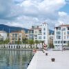 Beautiful waterfront buildings in Tivat, Montenegro, with mountains and a cloudy sky.