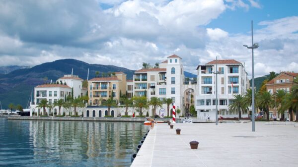 Beautiful waterfront buildings in Tivat, Montenegro, with mountains and a cloudy sky.