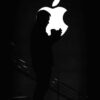 Silhouetted man against bright Apple logo, creating dramatic contrast.