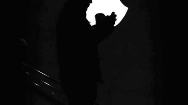 Silhouetted man against bright Apple logo, creating dramatic contrast.
