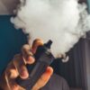 Hand holding a vaping device with a large cloud of smoke, indoors.
