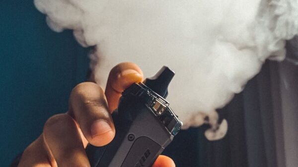 Hand holding a vaping device with a large cloud of smoke, indoors.