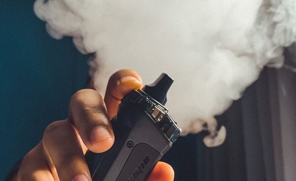 Hand holding a vaping device with a large cloud of smoke, indoors.