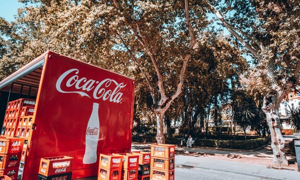 Coca-Cola truck unloading crates on a sunny street in Seville, Spain.