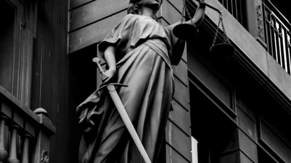 A dramatic black and white photo of a justice statue holding a sword and scales.