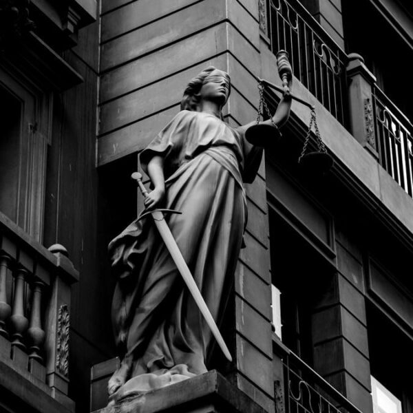 A dramatic black and white photo of a justice statue holding a sword and scales.