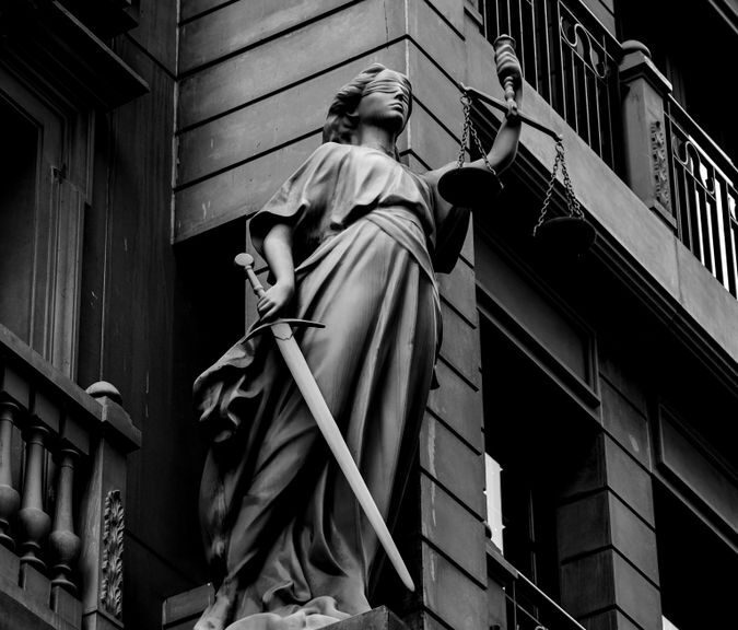 A dramatic black and white photo of a justice statue holding a sword and scales.