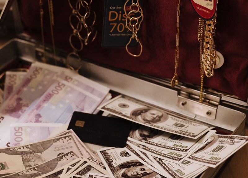 Open suitcase filled with cash, gold necklaces, and a sale tag, symbolizing wealth.