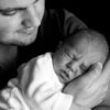 A touching black and white portrait of a father holding his sleeping newborn baby.