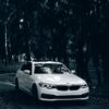 A stylish white BMW car driving through a serene forest path.
