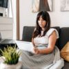 Woman on sofa with tablet and laptop, cozy home work environment.