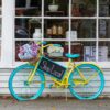 A colorful bicycle with flowers and 'Shop Local' sign outside a store in Sudbury, MA.